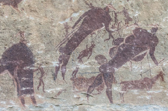 Cave wall painting of prehistoric hunters chasing animals with spears and bows, with silhouetted figures and deer silhouettes used for hunting scenes.