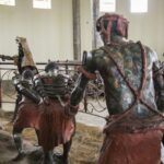 Life-size sculptures of robed figures inside a gallery, some tied with red ropes, surrounded by a metal railing.