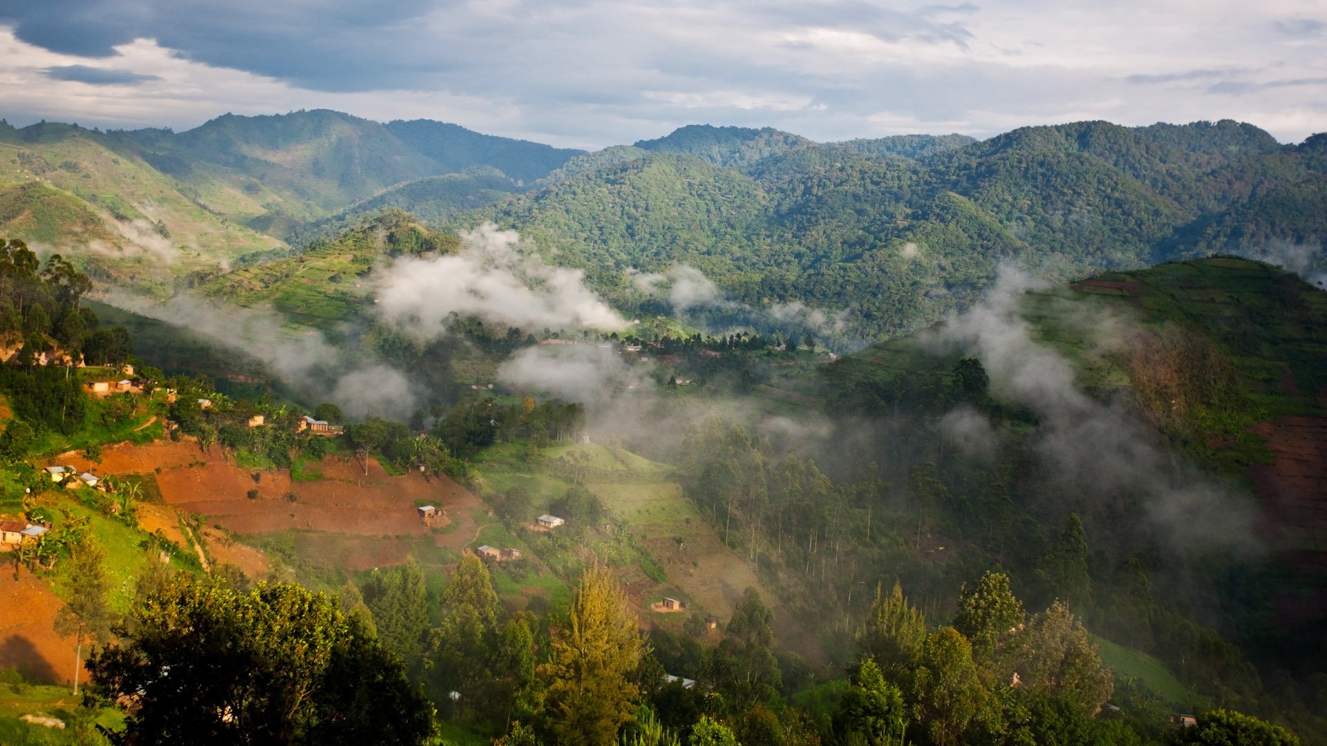 Mountain valley with terraced hills, scattered houses, and low-lying mist across the greenery.