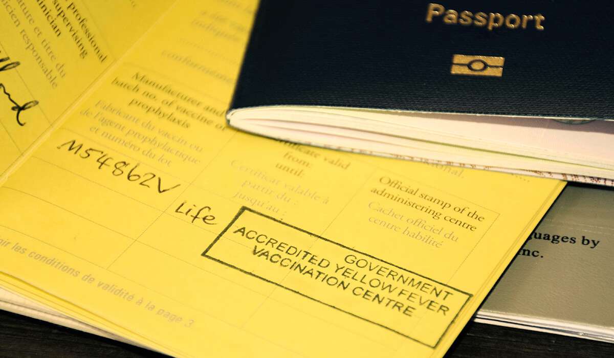Yellow vaccination cards with stamped text and a dark passport on top, showing a government yellow fever vaccination note