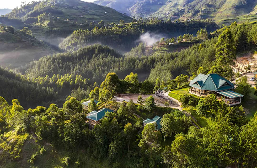A hillside resort with turquoise-roofed buildings surrounded by dense green forest and misty mountains.